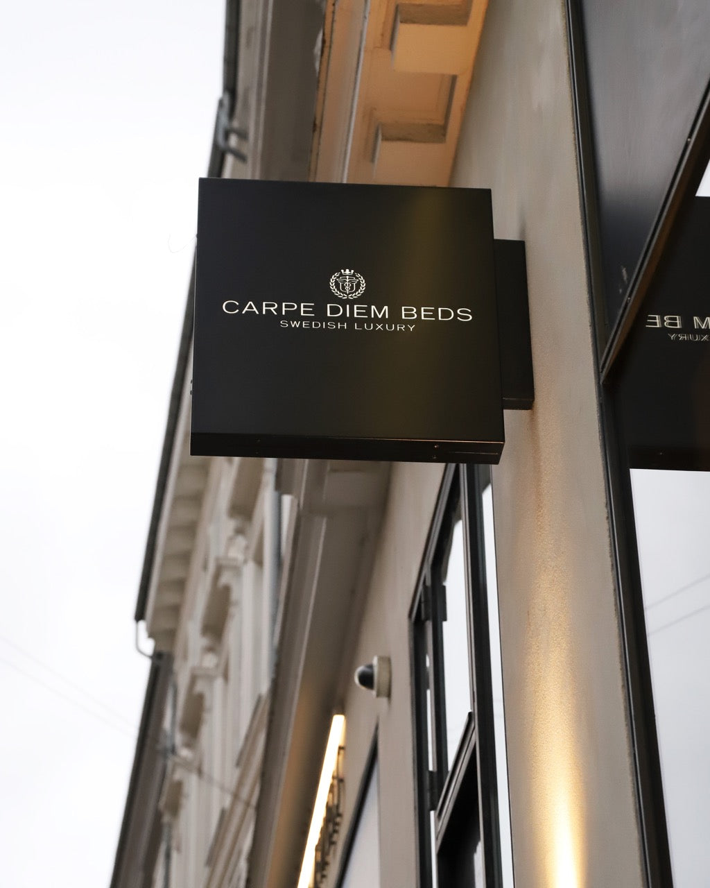 Black sign with 'Carpe Diem Beds' branding on a building facade.